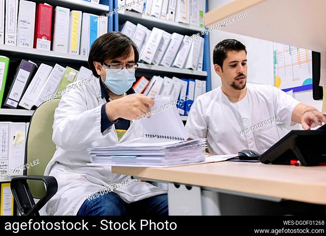 Male doctors doing paperwork on desk in pharmacy at hospital