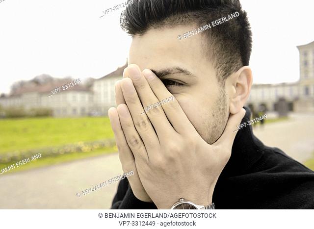 young Afghan man covering face with folded hands, in Munich, Germany