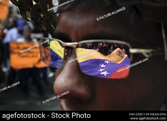 11 August 2022, Venezuela, Caracas: The Venezuelan flag is reflected on the glasses of a student during a protest against the government of President Maduro and...