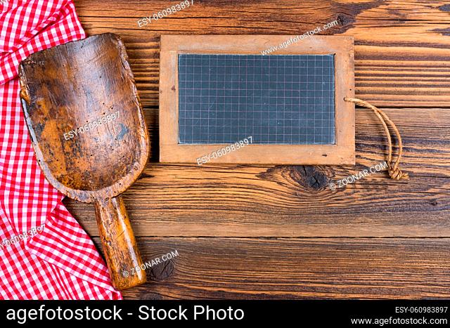 An old slate board and an old flour shovel as well as a red and white chequered cloth lie on a rustic wood background with space for text to design by yourself