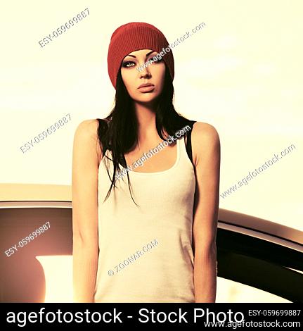 Young fashion hipster woman in white tank top and red beanie standing beside her car