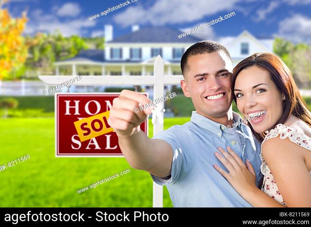 mixed-race excited military couple in front of new home with new house keys and sold real estate sign outside