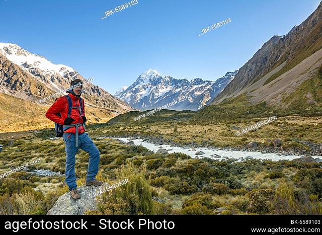 Hiker standing on a rock, Hooker Valley overlooking snow-capped Mount Cook, Hooker River, snow-capped Mount Cook National Park, Southern Alps, Canterbury