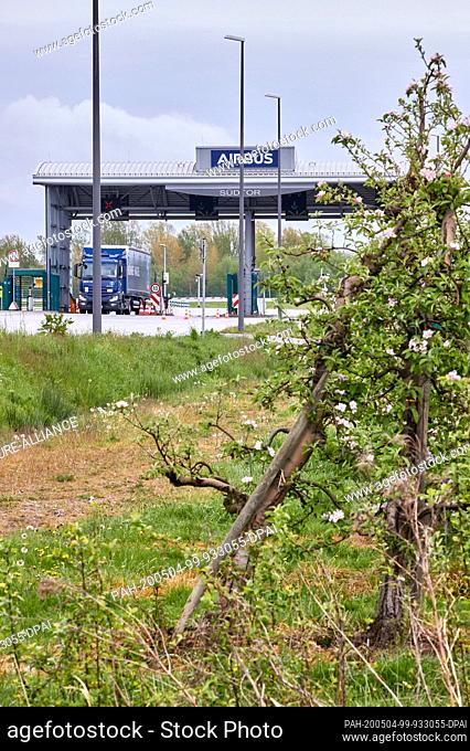 30 April 2020, Hamburg: Behind blossoming apple trees, the southern gate to the Airbus factory premises in Finkenwerder can be seen