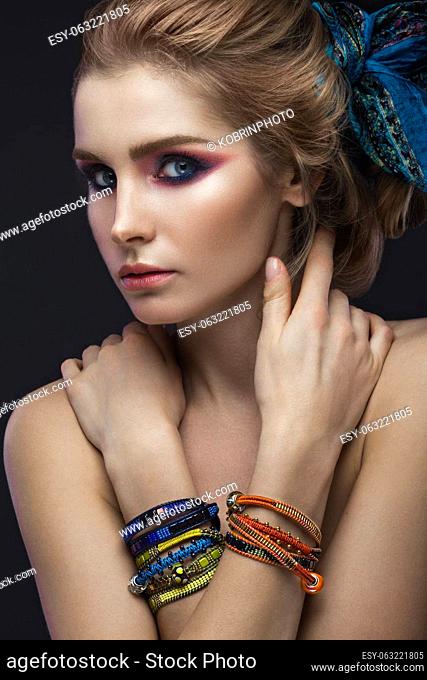 Beautiful fashion girl in a scarf and bracelets boho style. Beauty face, bright trendy makeup. Picture taken in the studio