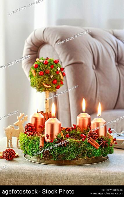 Christmas decoration in tree shape with moss, cinnamon sticks and rose hip and advent wreath on the table. Festive decor