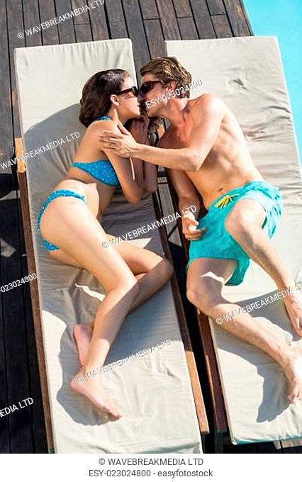 Romantic couple about to kiss on sun loungers