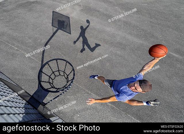 Young man dunking ball in hoop while playing basketball on sunny day