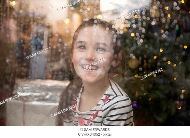 Portrait happy girl at wet window in Christmas living room