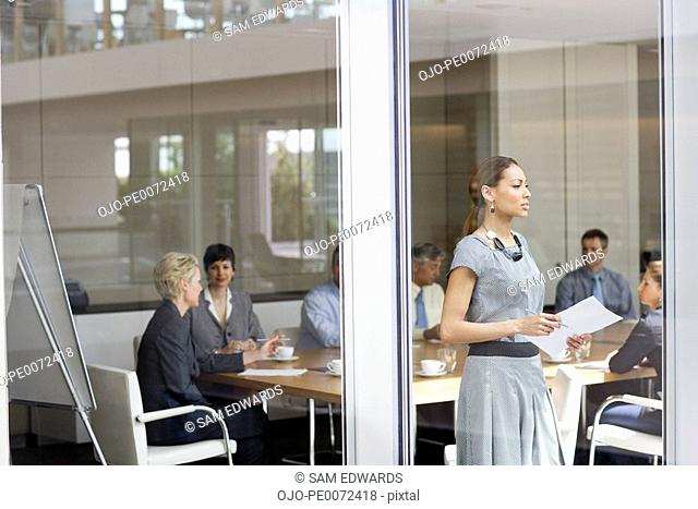 Businesswoman with paperwork looking out conference room window
