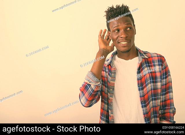 Studio shot of young happy black African man smiling while thinking and listening against white background