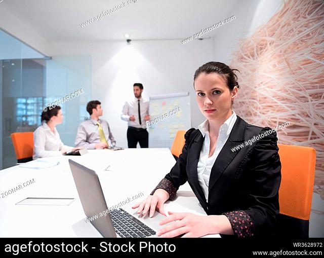 young business woman on meeting usineg laptop computer, blured group of people in background at modern bright startup office interior taking notes on white flip...
