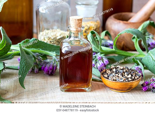 Comfrey tincture with dried root and fresh plant in the background