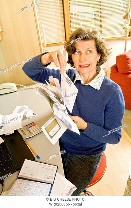 Frustrated woman sorting bills in home office