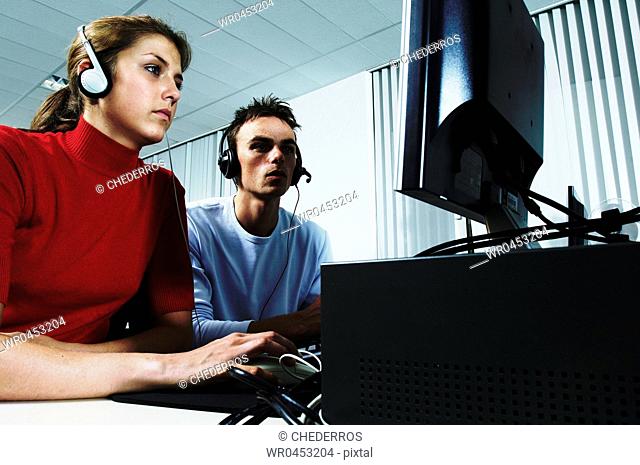 Teenage girl wearing headphones using a computer with a teenage boy sitting beside her