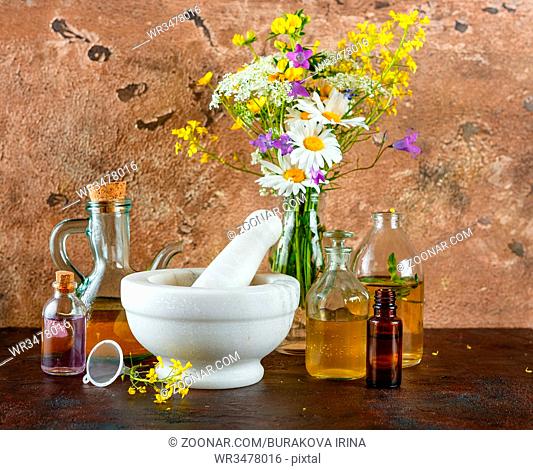 Mortar with fresh wild flowers and essential oil in glass bottles