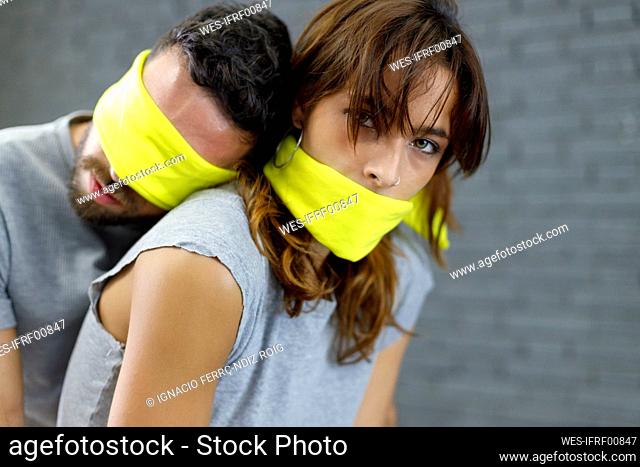 Blindfolded boyfriend leaning on girlfriend mouth covered with fabric