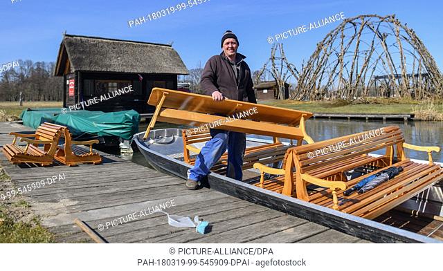 19 March 2018, Germany, Schlepzig: Ferryman Frank Seemann carries a table onto his Spreewald boat. While the water in the harbour is still covered with a thin...