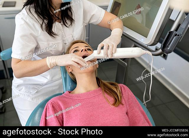 Dentist using dental camera for scanning teeth of patient at dental clinic