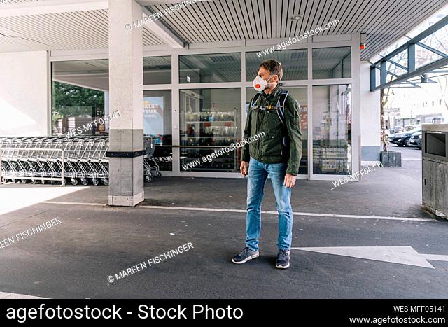 Man with mask standing outside supermarket