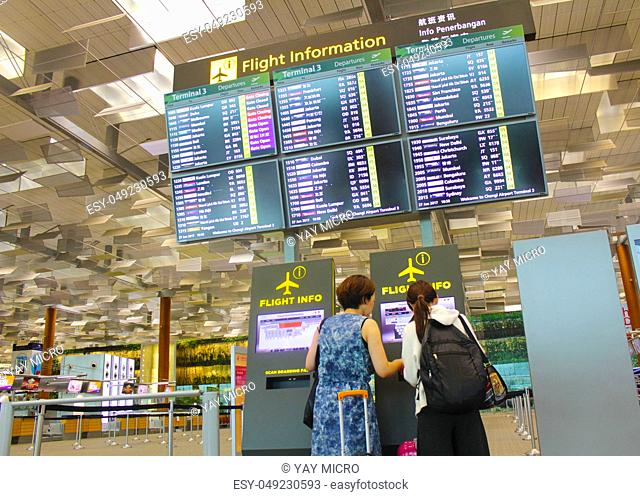Singapore - Jun 27, 2017 : Flights information board and machine at Changi airport terminal 3.Young girl with her mother touching self check in kiosks...