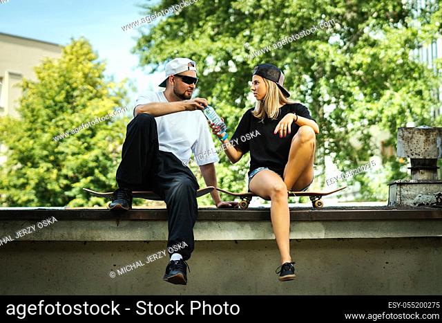 boy and girl on skateboards sit and give themselves drinking water
