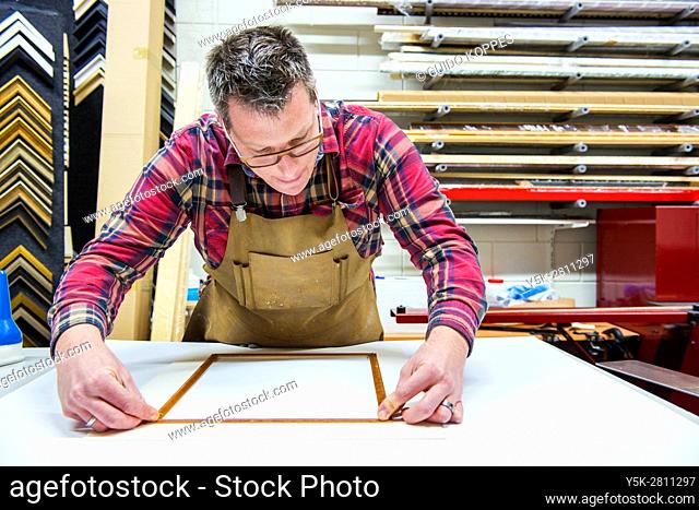 Goirle, Netherlands. Mid adult male craftsman and picture framemaker working on an assignment for a custiomer inside his workshop