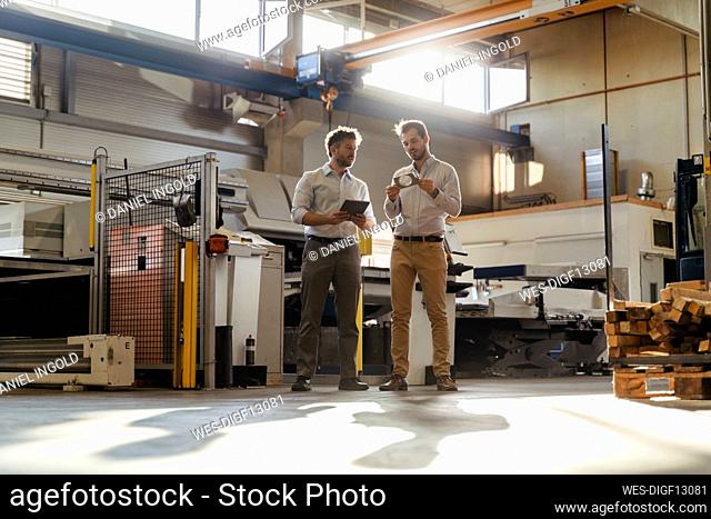 Businessman with digital tablet standing by colleague checking metal object at factory