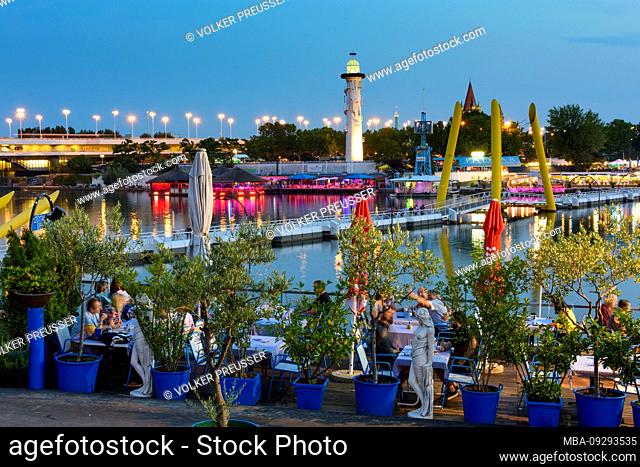 Wien / Vienna, river Neue Donau (New Danube), open air restaurant and bar at Copa Cagrana (front) and Sunken City (back), island Donauinsel, bridge Reichsbrücke