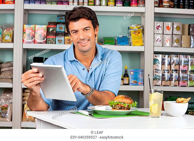 Portrait of mid adult male customer with snacks at table using digital tablet in supermarket