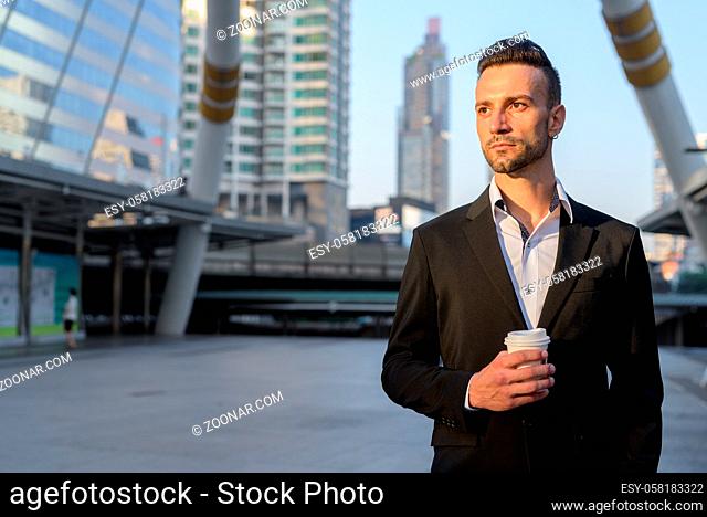 Portrait of handsome young Italian businessman outdoors in city wearing suit