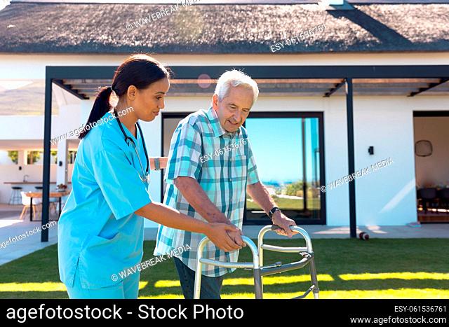 Biracial female health worker helping caucasian senior man to walk with a walking frame