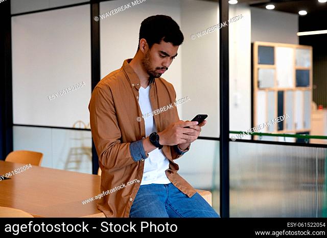 Mixed race businessman texting on smartphone in creative office