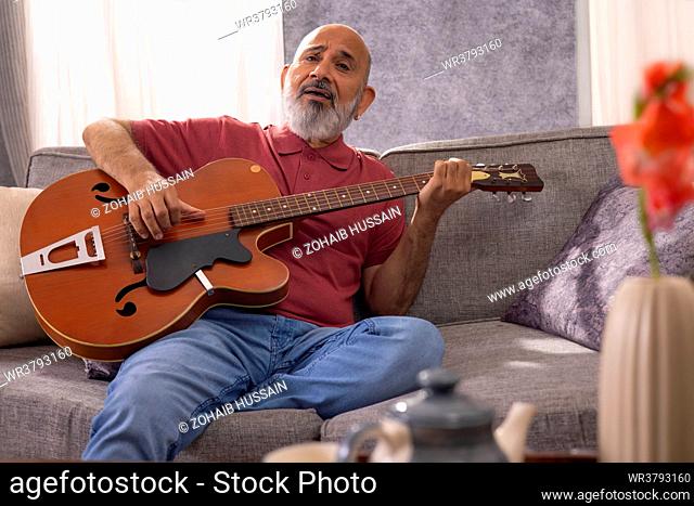 Portrait of senior man playing guitar while sitting on sofa at home