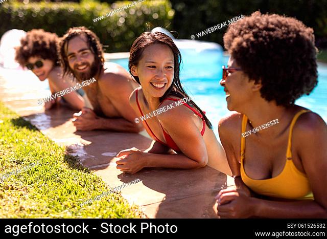 Diverse group of friends smiling and leaning on the poolside