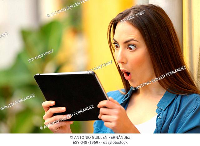 Surprised woman checking content on tablet outdoors in a colorful street
