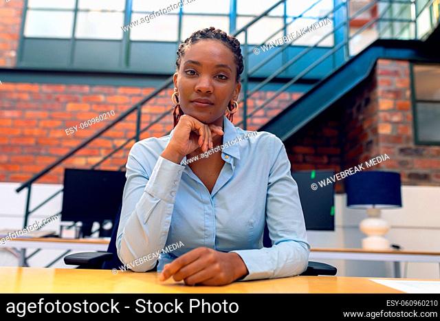 Portrait of confident african american young businesswoman with hand on chin at desk in office