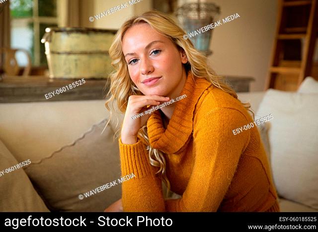 Portrait of happy caucasian woman sitting on couch in luxury living room, leaning on hand, smiling