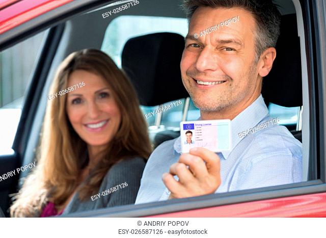 Happy Man Sitting Inside The Car With His Wife Showing Driving License