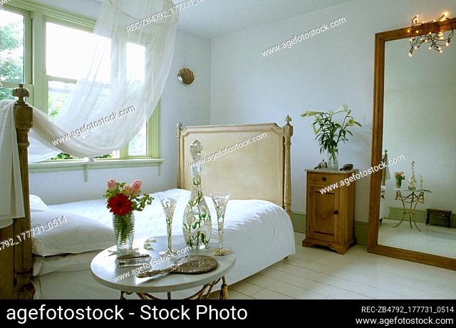 Romantic bedroom with sheer canopy over a double bed, large mirror, bedside table, and a sunny window
