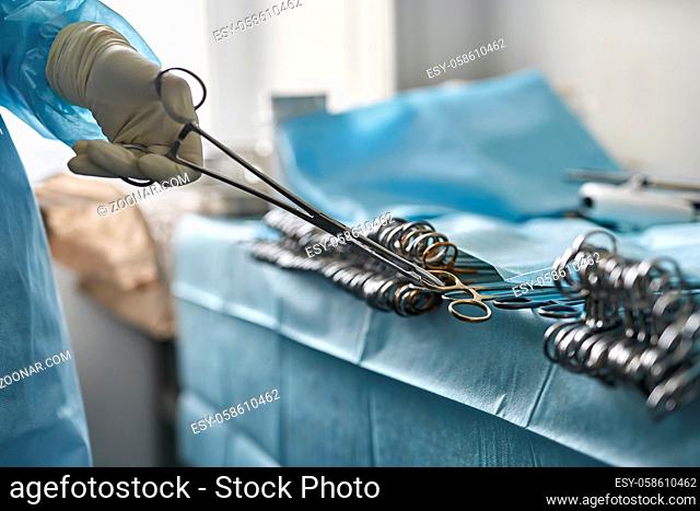 Nurse in medical glove is taking a surgical forceps from the table in the operating room. Closeup low aperture photo. Horizontal