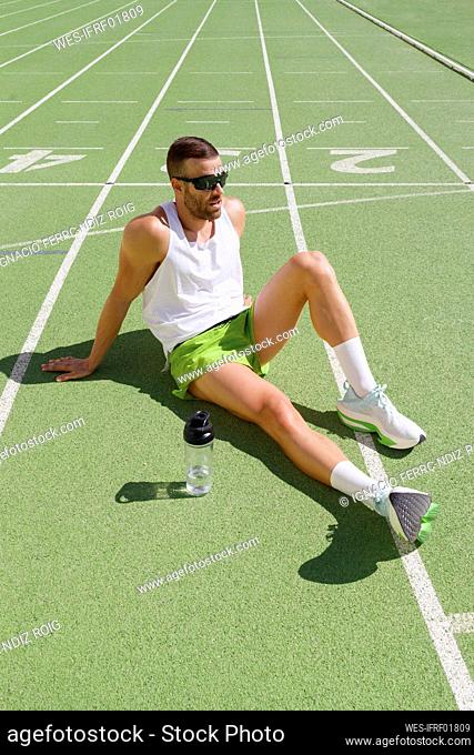 Tired athlete wearing sunglasses relaxing on sports track