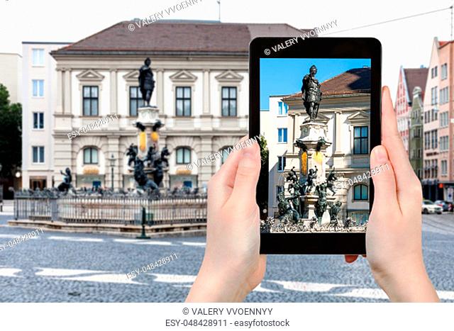 travel concept - tourist photographs of Augustusbrunnen (Augustus) fountain on Rathausplatz square in Augsburg city in Germany on smartphone