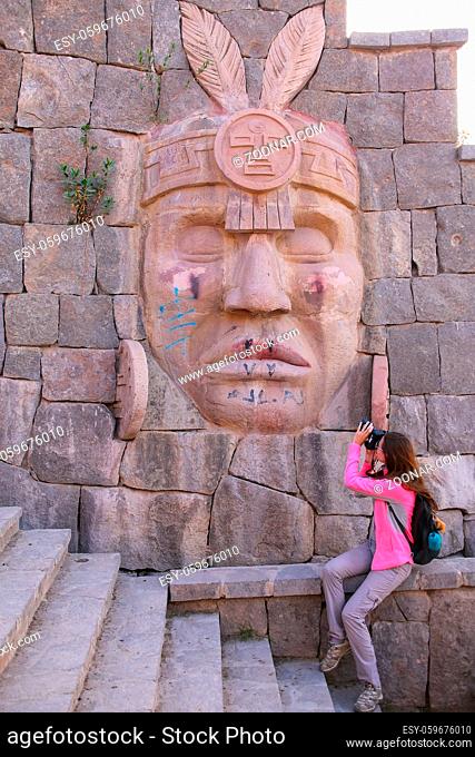 Woman photographing carving of Inca warrior on a wall in Chivay town, Peru. Chivay is the capital of Caylloma province
