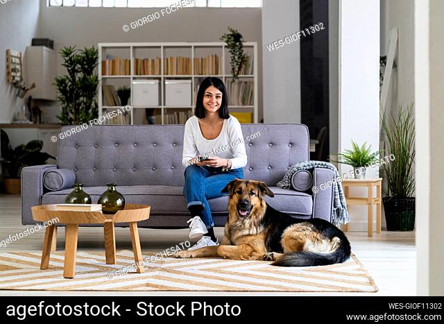 Smiling young woman with pet dog in living room