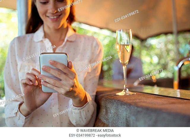 Smiling woman using mobile phone while having a glass of champagne