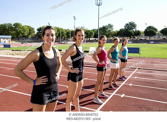 Smiling female runners standing on tartan track at starting line