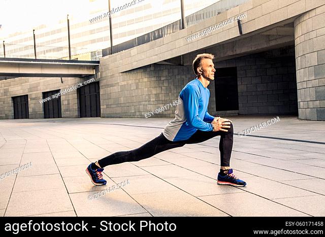 Handsome athlete man in black blue sport uniform stretching body, warming up and get ready for jogging