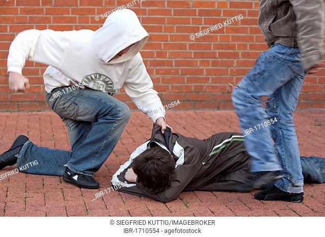 A defenseless boy lying on the ground while being held, kicked and beaten by two others, posed scene