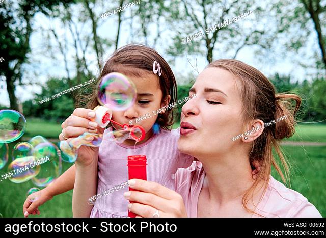 Daughter and mother blowing bubbles at park